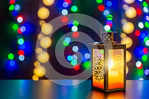 Candlestick with glowing candle is on the shiny table/background. Different colors lights are on the background.