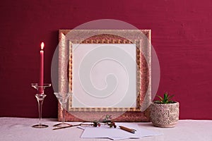 Candlestick on a long leg with a burning candle, houseplant, old photo frame on a red background