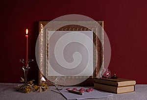 Candlestick on a long leg with a burning candle, old books, old photo frame on red and decor background
