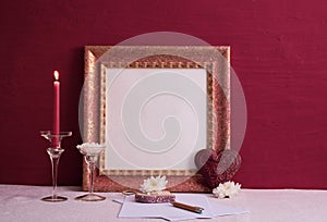 Candlestick on a long leg with a burning candle, stone heart, old photo frame on a red background