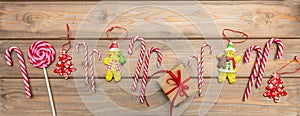 Candy canes, christmas ornaments and a gift box with red ribbon on wooden background, banner, top view