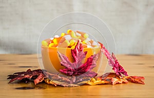 Candy corn in an orange bowl with autumn leaves on a wooden table