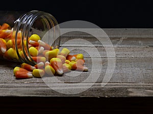 Candy Corn spilling out of a glass jar on a wood table