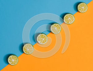 Candy hard bombon sliced lime fruits alligned in diagonal againts pastel blue and orange flat lay composition