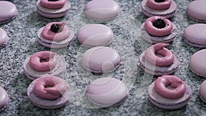 Candy store. Decoration of the French macaroons. The worker of a candy store in gloves adds cream and berries to a ready