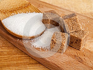 Cane sugar in cubes and ordinary white sugar scattered on a wooden spoon, close-up, types of sugars for food