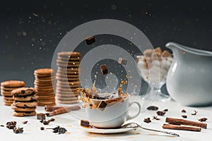 Cane sugar cubes splashing in cup with hot black coffee in front of biscuits