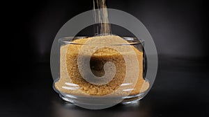 Cane sugar in a glass bowl on a black background.