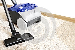 Canister modern vacuum cleaner blue for cleaning the house on the background of a soft beige carpet.