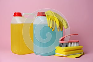 Canisters of cleaning supplies and tools on pink background