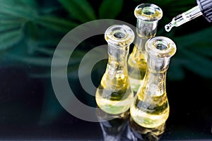 Cannabis oil/Cannabidiol on clear glasses on green marijuana leafs paper background.