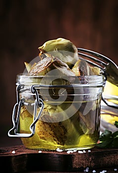 Canned artichokes in olive oil, in glass jar, rustic wooden kitchen table background, still life, sfallow DOF selective focus