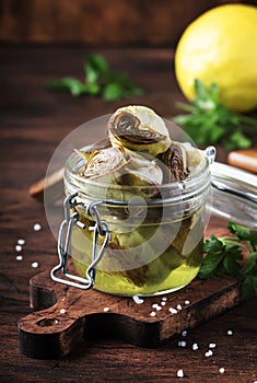 Canned artichokes in olive oil, in glass jar, rustic wooden kitchen table background, still life, sfallow DOF selective focus