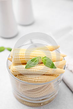 Canned baby corns with basil on light grey table, closeup