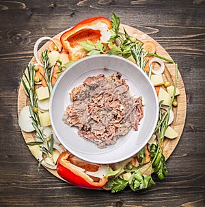 Canned beef white plate around lie ingredients vegetables and herbs on wooden rustic background top view