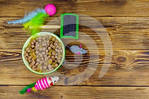 Canned cat food in bowl, cat toys and pet slicker brush on wooden background. Top view, copy space. Pet care concept