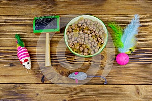 Canned cat food in bowl, cat toys and pet slicker brush on wooden background. Top view. Pet care concept