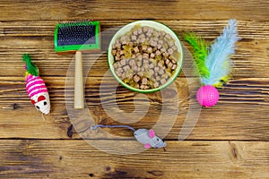 Canned cat food in bowl, cat toys and pet slicker brush on wooden background. Top view. Pet care concept