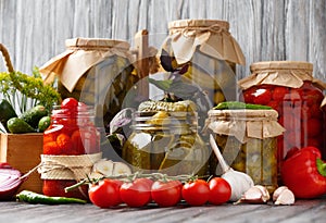Canned cherry tomatoes and cucumbers in jars on a wooden background