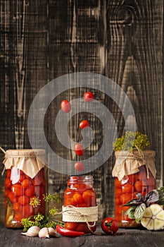 Canned cherry tomatoes fall into a jar on a wooden background with space for text