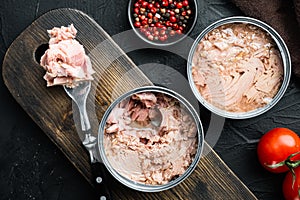 Canned Chunk Light Tuna, on wooden cutting board, on black background with herbs and ingredients, top view flat lay