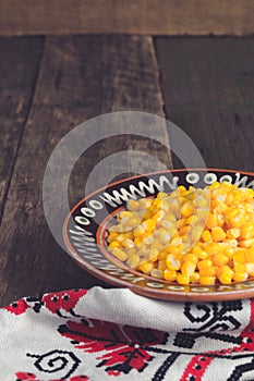 Canned corn in a brown bowl on wooden background near tablecloth. Copy space.