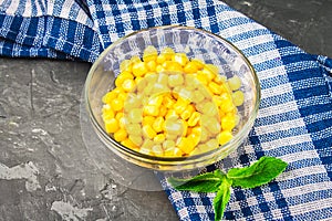 Canned corn in a glass plate on a gray concrete background.