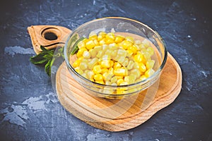 Canned corn in a glass plate on a gray concrete background.