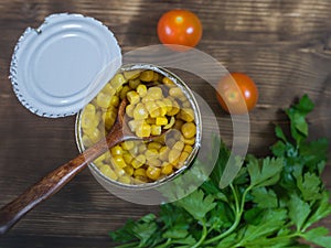 Canned corn in an open aluminum cans and parsley on a wooden table. The view from the top.