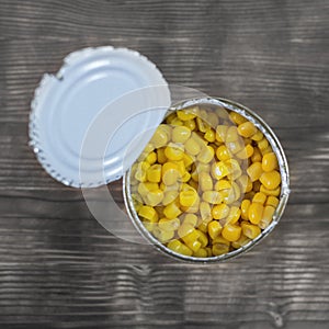 Canned corn in an open aluminum cans on a wooden table. The view from the top.