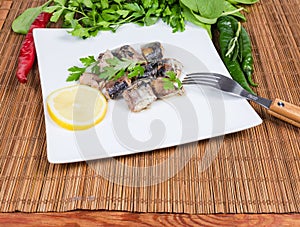 Canned fish on dish with fork among vegetables and greens