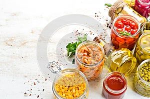 Canned food in glass jars on white wooden background.