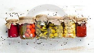 Canned food in glass jars on white wooden background.