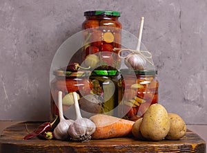 Canned food at home. Canned Tomatoes and Pickles. Fresh vegetables carrots, potatoes and garlic on a gray background