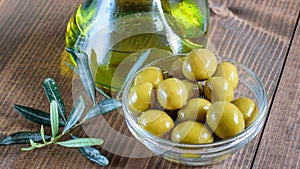 Canned green olives in glass bowl, olive oil bottle and olive tree branch on the wooden table closeup