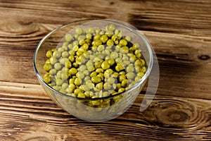 Canned green peas in glass bowl on wooden table