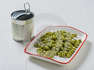 Canned green peas in a white plate and a tin can on a wooden table.
