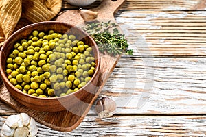 Canned green peas in a wooden bowl. Canned food. White background. Top view. Copy space