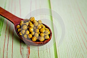 Canned green peas in a wooden spoon lying on a wooden surface of green color