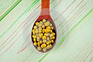 Canned green peas in a wooden spoon lying on a wooden surface of green color