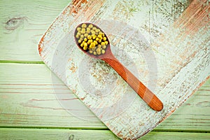 Canned green peas in a wooden spoon lying on a wooden surface of green color