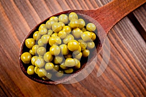 Canned green peas in a wooden spoon lying on a wooden surface of the table