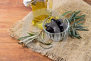 Canned olives in bowl against olive branch and olive oil