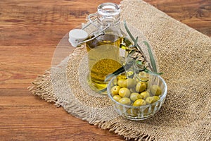 Canned olives in bowl against olive branch and olive oil