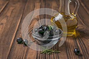 Canned olives in a glass bowl and a bottle of olive oil on a wooden table.