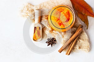 Canned organic pumpkin puree in glass jar with fresh pumpkin, cinnamon and anise on light stone background. Ingredient for