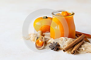 Canned organic pumpkin puree in glass jar with fresh pumpkin, cinnamon and anise on light stone background. Ingredient for