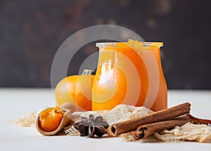 Canned organic pumpkin puree in glass jar with fresh pumpkin, cinnamon and anise on light stone background. Ingredient for