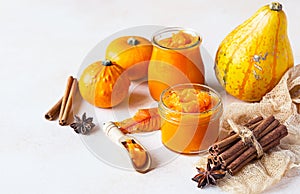 Canned organic pumpkin puree in glass jar with fresh pumpkin, cinnamon and anise on light stone background. Ingredient for