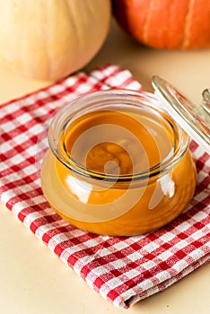 Canned Organic Pumpkin Puree in Glass Jar with Fresh Pumpkin Napkin Yellow Background Thanksgiving Autumn or Winter Recipes